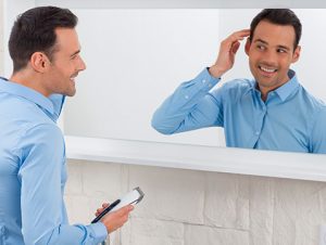 mężczyzna uśmiecha się do lustra podczas podgalania włosów maszynką do strzyżenia